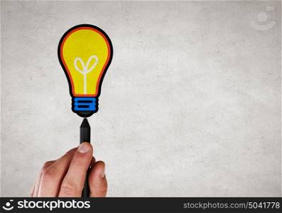 Outline your idea. Close up of hand drawing light bulb with marker