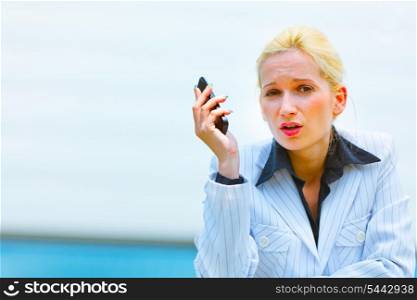 Outraged modern business woman with cell phone leaning on railing at office building&#xA;