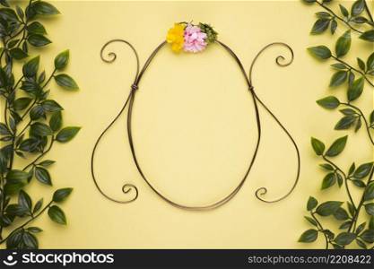 oval shape frame with artificial rose yellow wall with green leaves