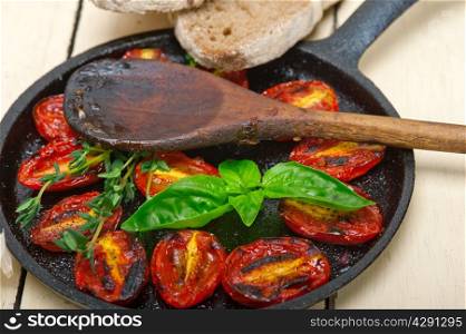 oven baked cherry tomatoes with basil and thyme on a cast iron skillet and wood spoon