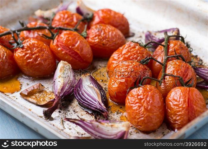 Oven roasted onions and tomatoes on metal baking tray, top view, selective focus