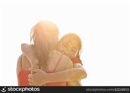 Over the shoulder sunlit view of girl hugging mother