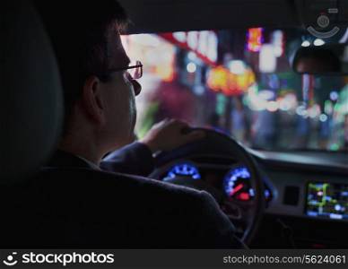 Over the shoulder view of businessman driving at night in the city, illuminated city lights