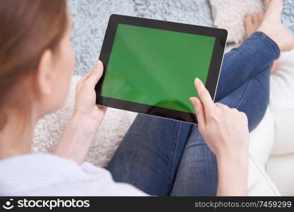 Over The Shoulder View Of Woman Lying On Sofa Using Green Screen Digital Tablet At Home