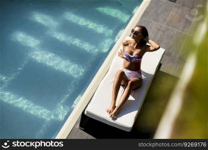 Over view at beautiful tanned woman with sunglasses in bikini relaxing near luxury swimming pool