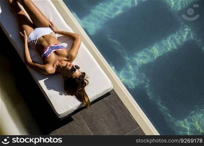 Over view at beautiful tanned woman with sunglasses in bikini relaxing near luxury swimming pool