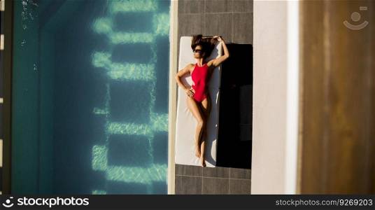 Over view at beautiful tanned woman with sunglasses in red bikini relaxing near luxury swimming pool