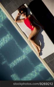 Over view at beautiful tanned woman with sunglasses in red bikini relaxing near luxury swimming pool