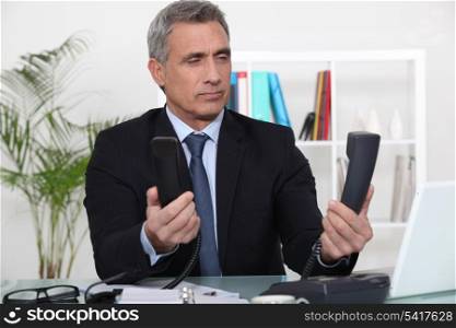 Over worked businessman holding two telephones