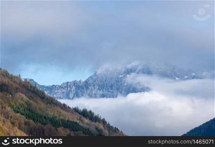 Overcast autumn alpine view with famous Bavarian mount Watzmann silhoette fragments through fog and clouds, Berchtesgadener Land, Bavaria, Germany. Climate, environment and weather concept sky background.