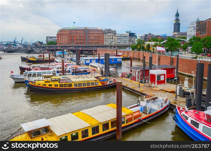 Overcast skyline of Hamburg harbor with moored touristic boats by the piers, freight cranes of industrial shipping city port on background, Germany