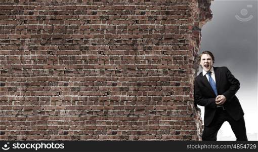 Overcoming barriers. Young businessman making effort to move brick wall