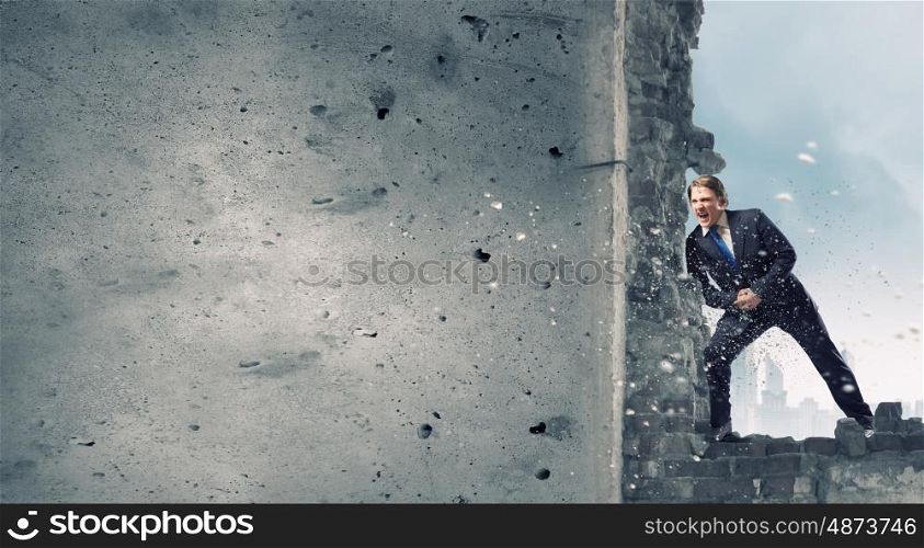 Overcoming barriers. Young businessman making effort to move brick wall