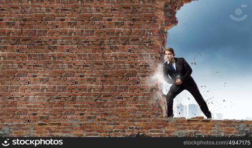 Overcoming barriers. Young businessman making effort to move brick wall