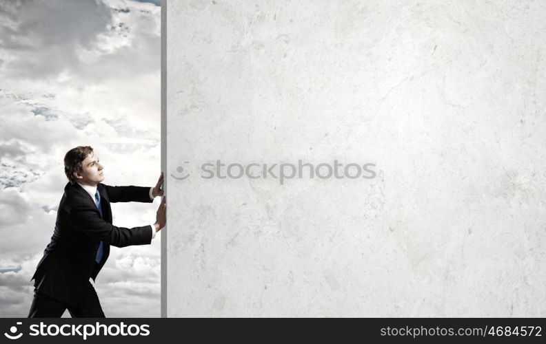 Overcoming barriers. Young businessman making effort to move stone wall