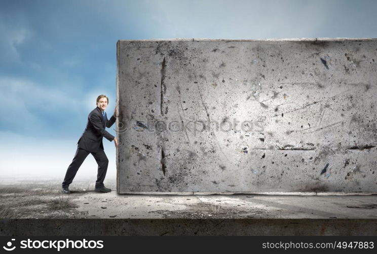 Overcoming barriers. Young businessman making effort to move stone wall
