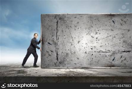Overcoming barriers. Young businessman making effort to move stone wall
