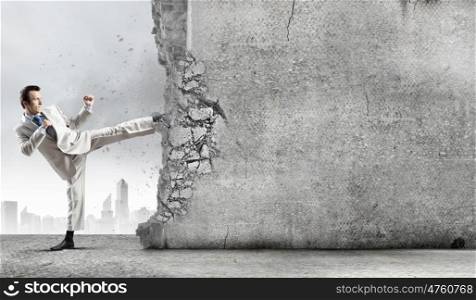 Overcoming challenges. Businessman breaking stone wall with karate kick