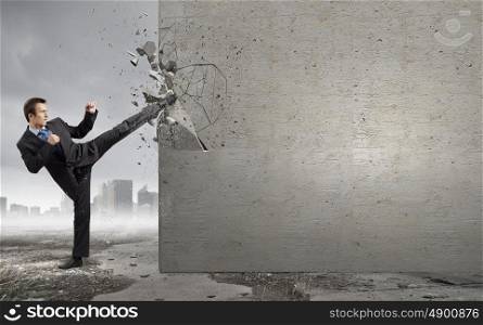 Overcoming challenges. Businessman breaking stone wall with karate kick