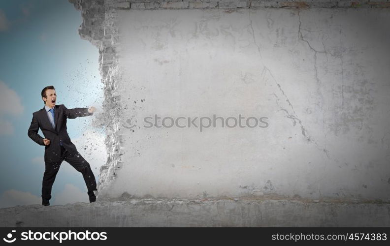 Overcoming challenges. Businessman breaking stone wall with karate punch