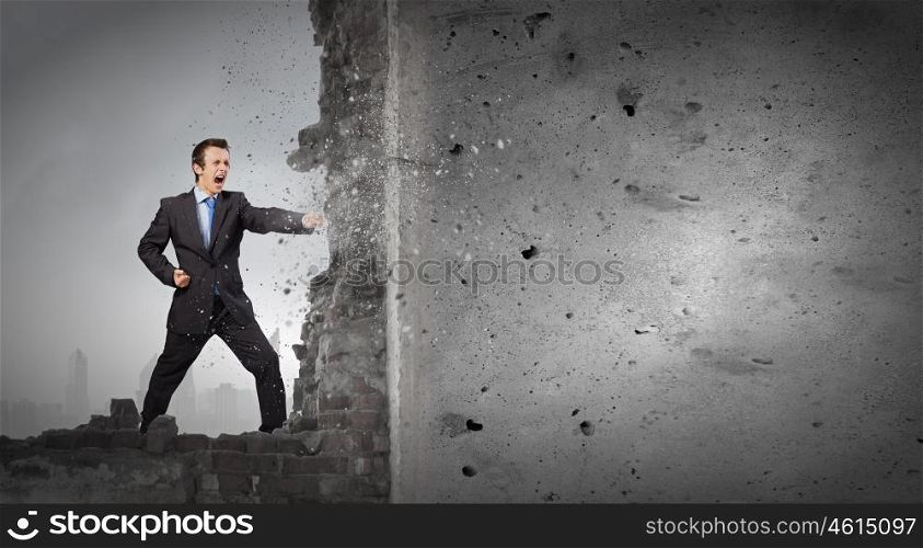 Overcoming challenges. Businessman breaking stone wall with karate punch