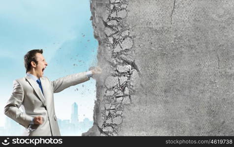 Overcoming challenges. Businessman breaking stone wall with karate punch