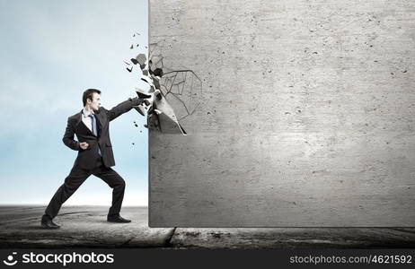 Overcoming challenges. Businessman breaking stone wall with karate punch