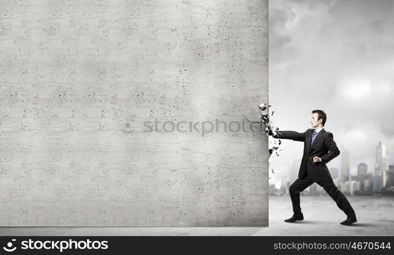 Overcoming challenges. Businessman breaking stone wall with karate punch