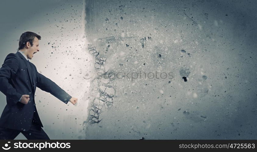 Overcoming challenges. Businessman breaking stone wall with karate punch