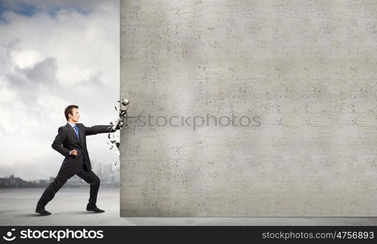 Overcoming challenges. Businessman breaking stone wall with karate punch