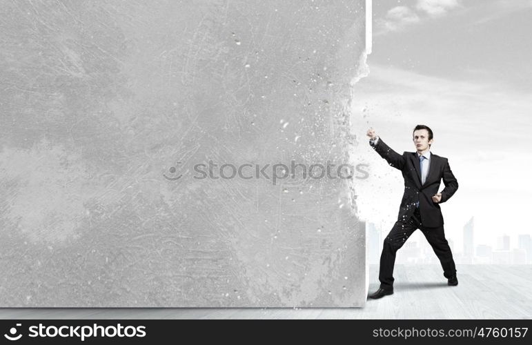 Overcoming challenges. Businessman breaking stone wall with karate punch