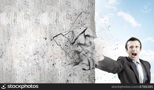 Overcoming challenges. Businessman breaking stone wall with karate punch