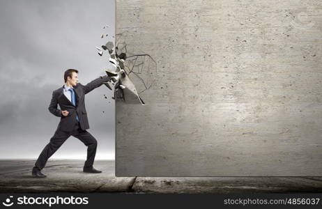 Overcoming challenges. Businessman breaking stone wall with karate punch