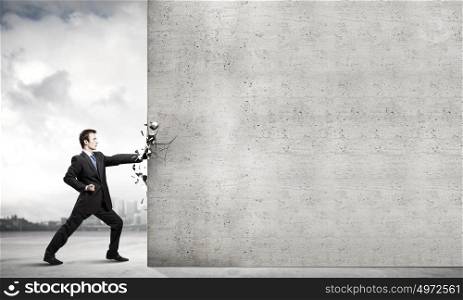 Overcoming challenges. Businessman breaking stone wall with karate punch