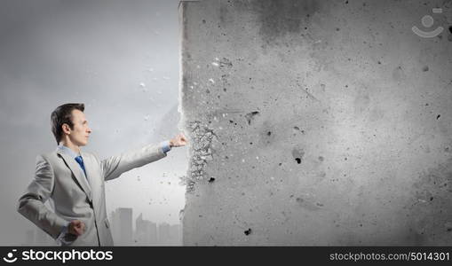 Overcoming challenges. Businessman breaking stone wall with karate punch