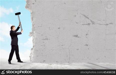 Overcoming challenges. Young businessman breaking cement wall with hammer