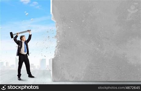 Overcoming challenges. Young businessman breaking cement wall with hammer