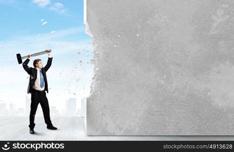 Overcoming challenges. Young businessman breaking cement wall with hammer