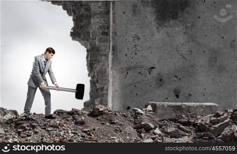 Overcoming challenges. Young businessman breaking old wall with hammer