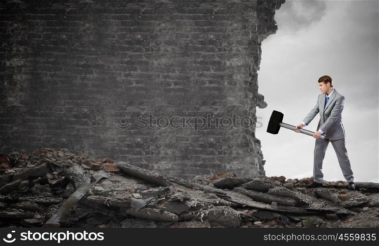 Overcoming challenges. Young businessman breaking old wall with hammer