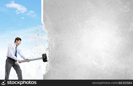 Overcoming challenges. Young businessman breaking old wall with hammer