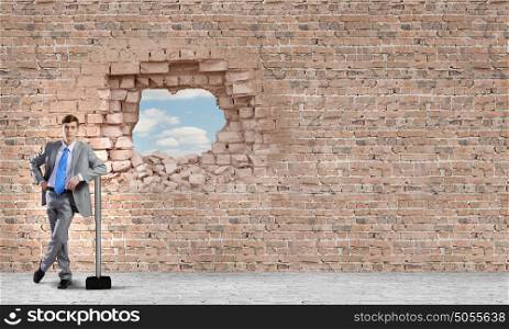 Overcoming challenges. Young businessman with big hammer against wall