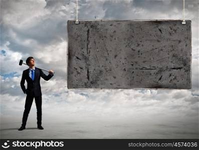Overcoming challenges. Young businessman with hammer in hands and cement banner. Place for text