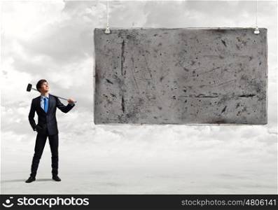 Overcoming challenges. Young businessman with hammer in hands and cement banner. Place for text