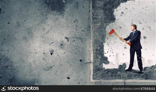 Overcoming challenges. Young determined businessman crashing wall with axe