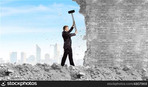 Overcoming challenges. Young determined businessman crashing wall with hammer