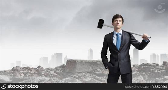 Overcoming challenges. Young determined businessman with hammer in hands