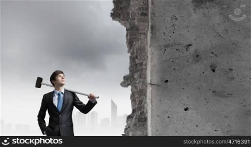 Overcoming challenges. Young determined businessman with hammer in hands