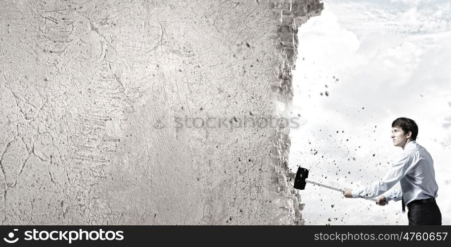 Overcoming challenges. Young determined businessman with hammer in hands