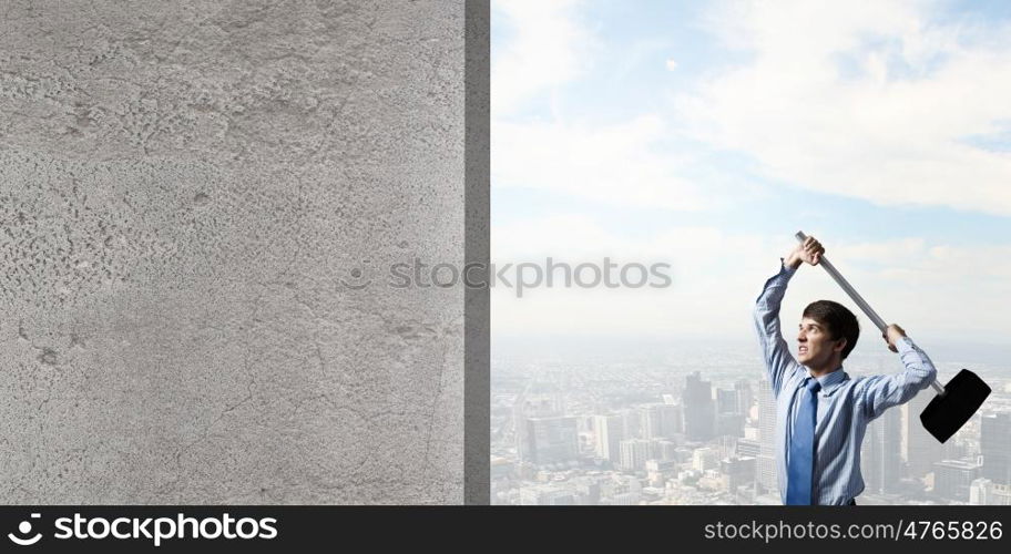 Overcoming challenges. Young determined businessman with hammer in hands